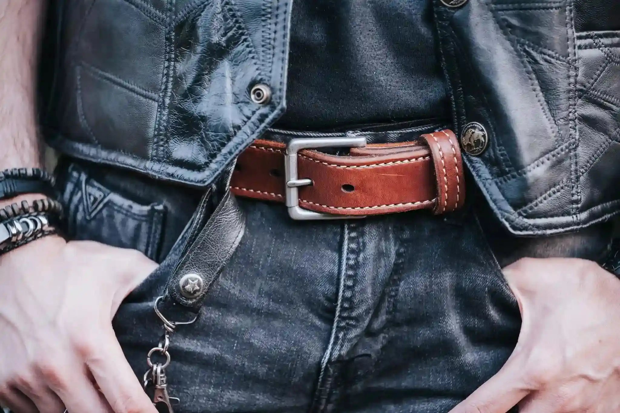Close-up of a person wearing a leather vest and jeans with a brown belt.